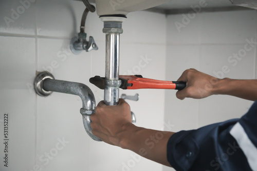 Male Plumber Using Wrench To Fix Leaking Sink In Home Bathroom.