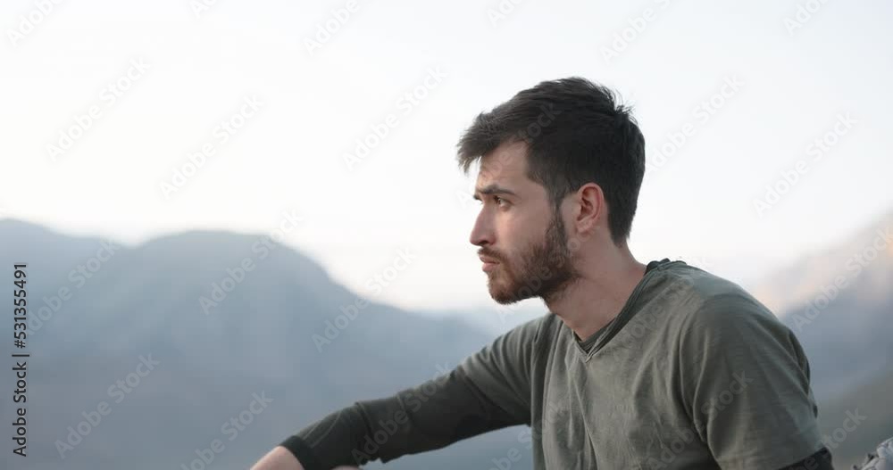 Close-up.A cool, cute young hipster, sitting on top of a mountain, thoughtfully looking into the distance at a beautiful sunset. A nomadic tourist, a travel blogger.The concept of freedom Close-up.A cool, cute young hipster, sitting on top of a mountain, thoughtfully looking into the distance at a beautiful sunset. A nomadic tourist, a travel blogger.The concept of freedom