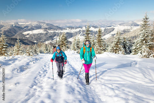 two girls with backpacks walk along a path in the winter mountains. hiking in the mountains. © zhukovvvlad