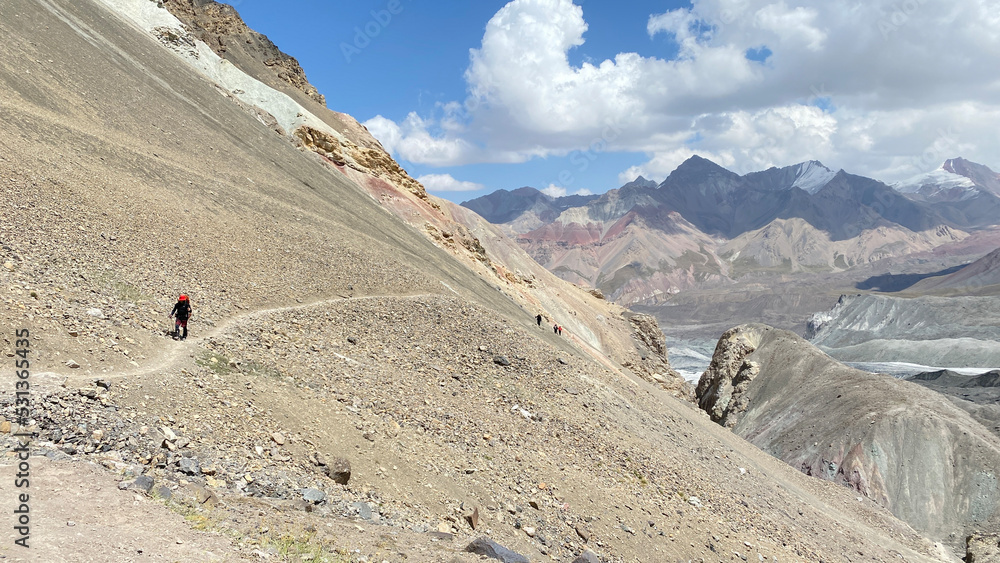 Several tourists are walking along a narrow mountain path. Beautiful mountain landscape. View of the mountains, colored rocks and hills of Kyrgyzstan.