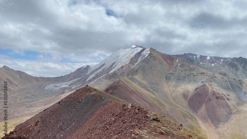 Multi-colored rocky mountains with snow-capped peaks. The amazing nature of the Pamirs. Beautiful summer mountain landscape.