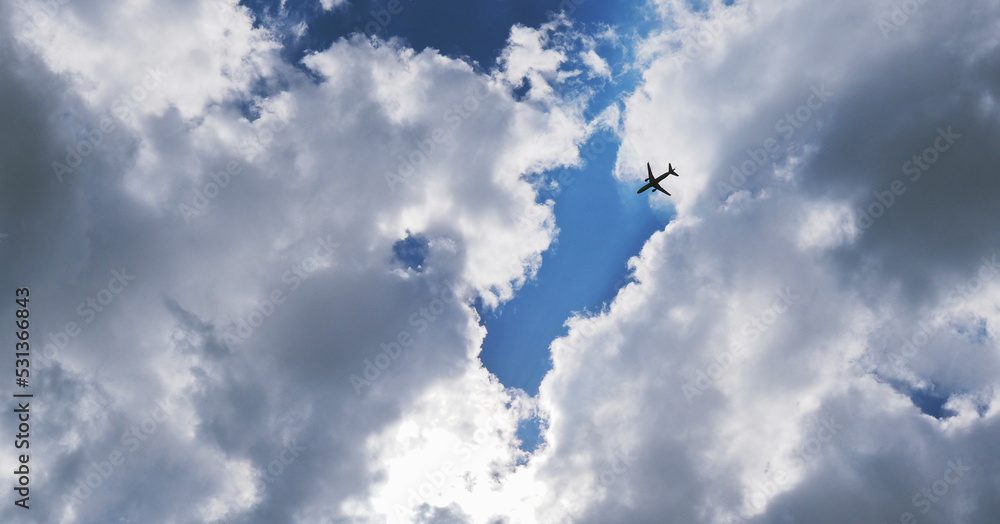 The passenger airplane is flying far away in the blue sky and clouds. Dramatic clouds with the sun shining through them. Aircraft in air. Horizontal stories. International passenger air transportation The passenger airplane is flying far away in the blue sky and clouds. Dramatic clouds with the sun shining through them. Aircraft in air. Horizontal stories. International passenger air transportation