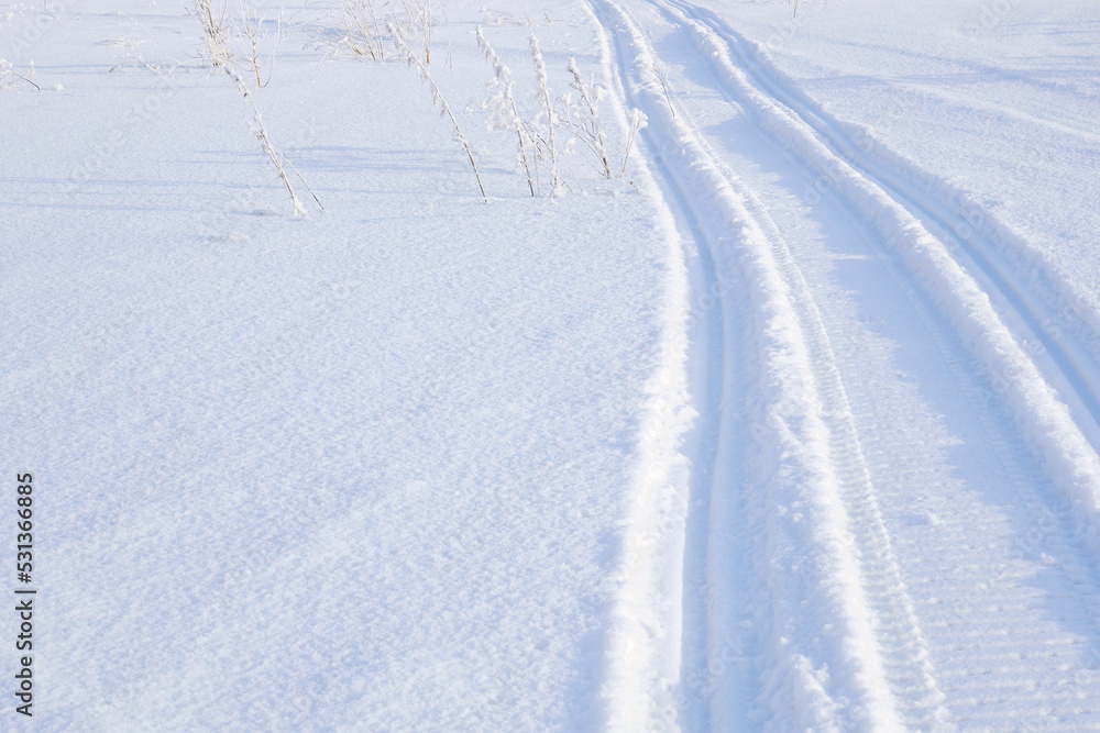 Track of traces from a snowmobile in drifts of white snow. Nature and outdoor on a winter sunny day. Background or wallpaper
