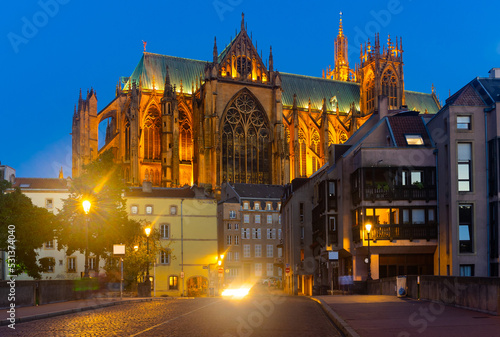 Picturesque view of Metz cityscape overlooking illuminated majestic Gothic Roman Catholic Cathedral of Saint Stephen dominating residential buildings against blue sky at summer twilight  France..