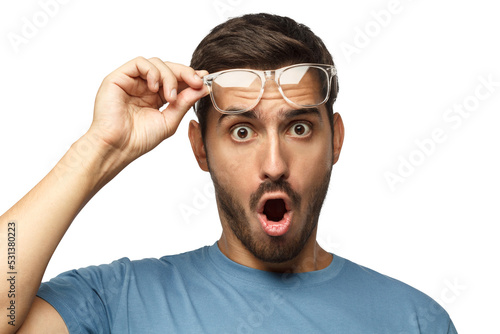 Young man in blue t-shirt shouting OMG with open mouth, surprised by low price and sales, holding transparent glasses photo