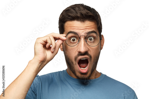 Angry young teacher in blue t-shirt shouting, displeased with bad behaviour, holding round eyeglasses with one hand