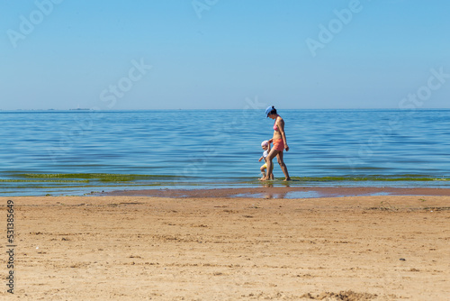 Mom and little two-year-old daughter are walking along the seashore along the beach