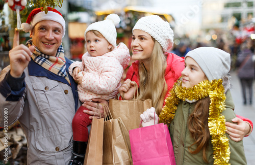 Smiling parents with their two nice daughters choosing Christmas toys at Christmas fair