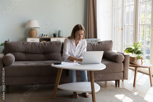 Serious millennial homeowner woman using online app on laptop for checking bills, paying mortgage, rent, insurance fees. Businesswoman, entrepreneur, freelance accountant working at home
