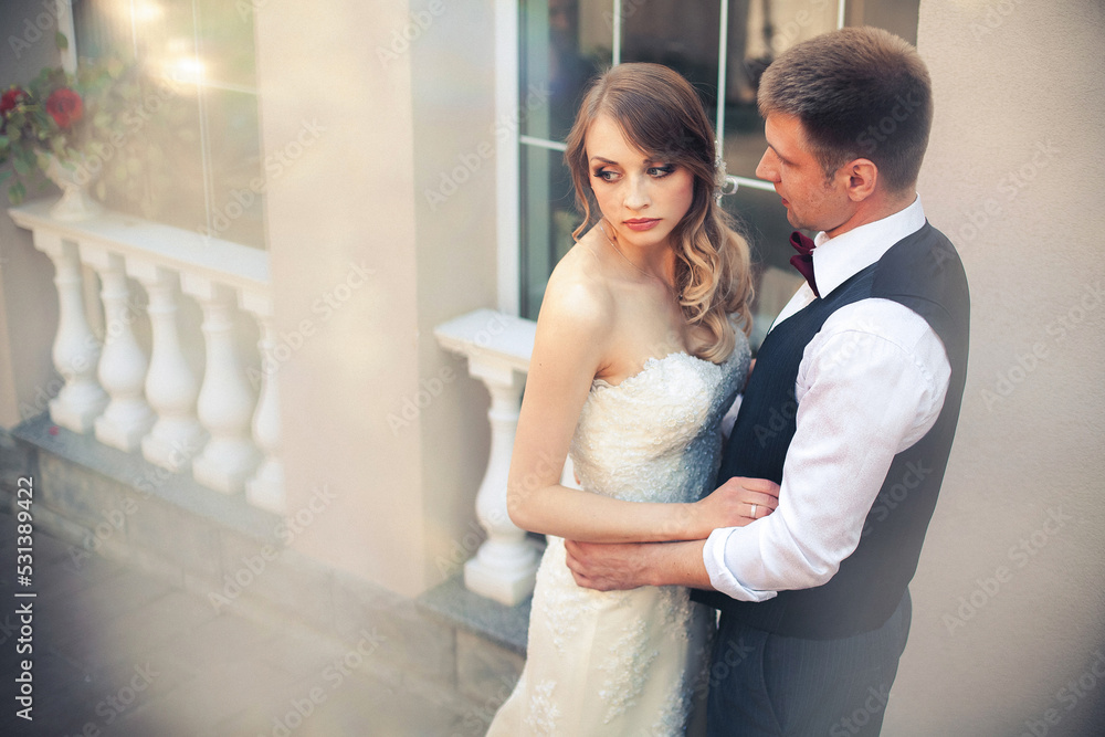 Art work. Stylish newlyweds hugging against the backdrop of the interior of the restaurant. The bride is dressed in a light wedding dress, the groom is dressed in a white shirt, jumper and bow tie.