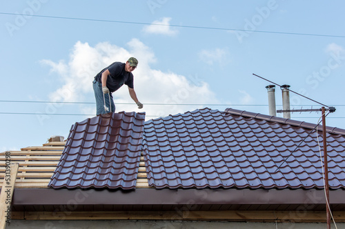 Workers install metal roofing on the wooden roof of a house.