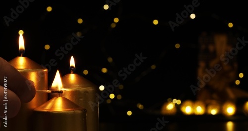 The fingers of the hand are squeezing a burning match that lights golden candles. Christmas card conveying the atmosphere of the holiday There is a place to insert congratulatory words. © Александр Лебедько