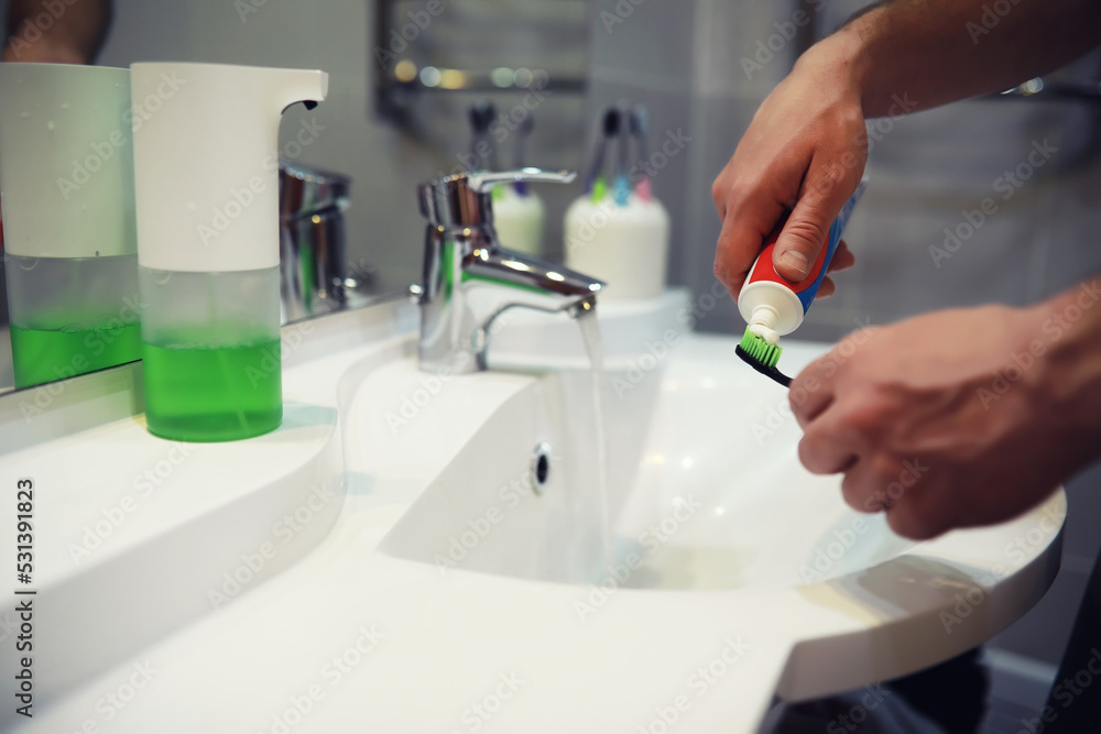 Hands with tooth brush and paste on blurred background in the bathroom in the sink. Selective focus. Hands with tooth brush and paste on blurred background in the bathroom in the sink. Selective focus.