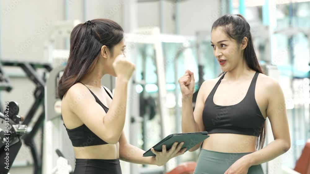 Two asian female personal trainer helping young woman and discussing together in gym. Two asian female personal trainer helping young woman and discussing together in gym.