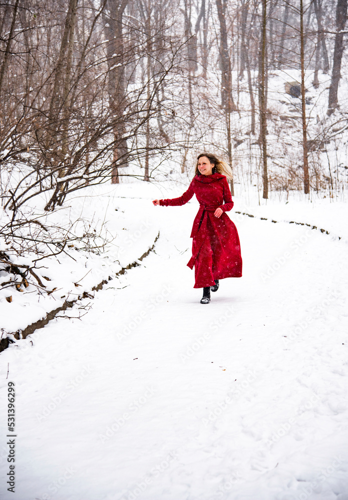 beautiful smiling happy woman in red long dress having fun with snow in winter forest