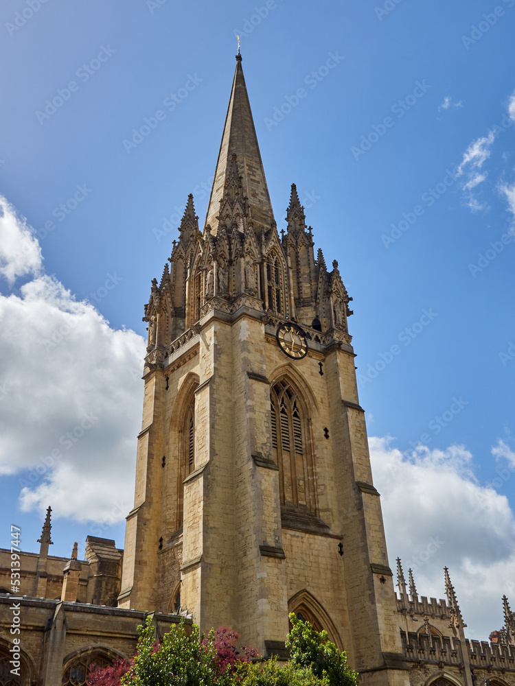 Fototapeta premium Tower of The University Church of St Mary the Virgin with a decorated spire with pinnacles and statues in a sunny day with fluffy white clouds. Oxford, England, UK Europe