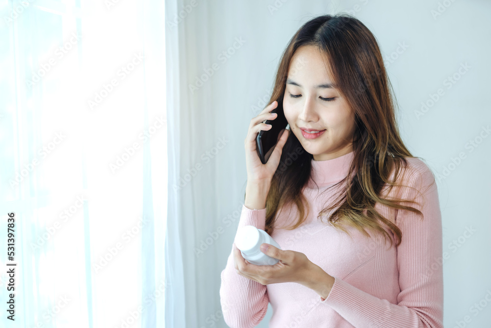 Young asian women checking pills while ordering online medicines on mobile phone at home - concept of E pharmacy, technology and healthcare Young asian women checking pills while ordering online medicines on mobile phone at home - concept of E pharmacy, technology and healthcare