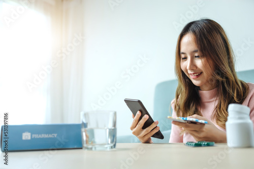 Young asian women checking pills while ordering online medicines on mobile phone at home - concept of E pharmacy, technology and healthcare