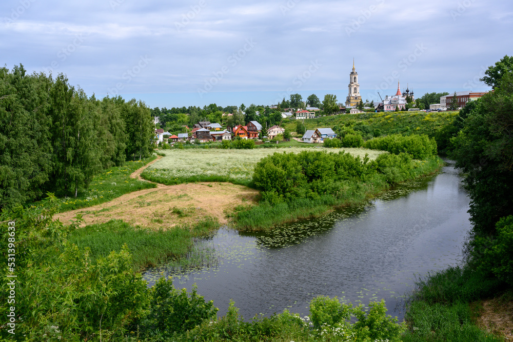 View of the pond, blooming meadow, forest, bell tower, churches and cottages in summer in Suzdal, Russia View of the pond, blooming meadow, forest, bell tower, churches and cottages in summer in Suzdal, Russia