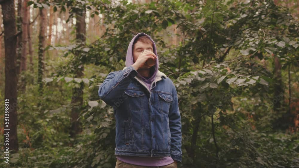 Young man in warm clothes drinking coffee from paper cup, standing in forest. Young man in warm clothes drinking coffee from paper cup, standing in forest.
