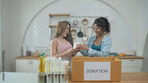 Volunteer concept of 4k Resolution. Asian women packing food in a donation box together at home. Consumer goods donated to help the victims. photo