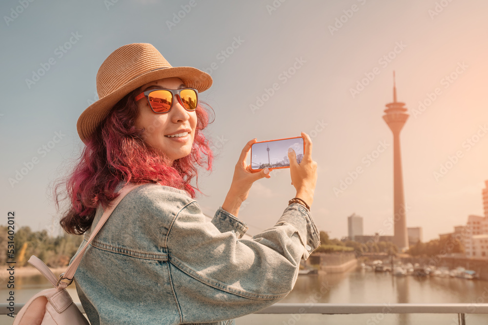 Happy girl travel blogger takes selfie pictures on her smartphone of the famous Dusseldorf TV tower from the Media Harbor canal in the post industrial district. Travel and sightseeing locations