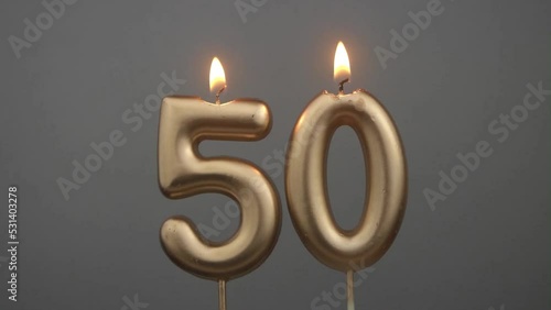 Burning gold birthday candles on gray background, number 50