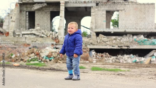 A little boy stands and cries, in the background a broken building
