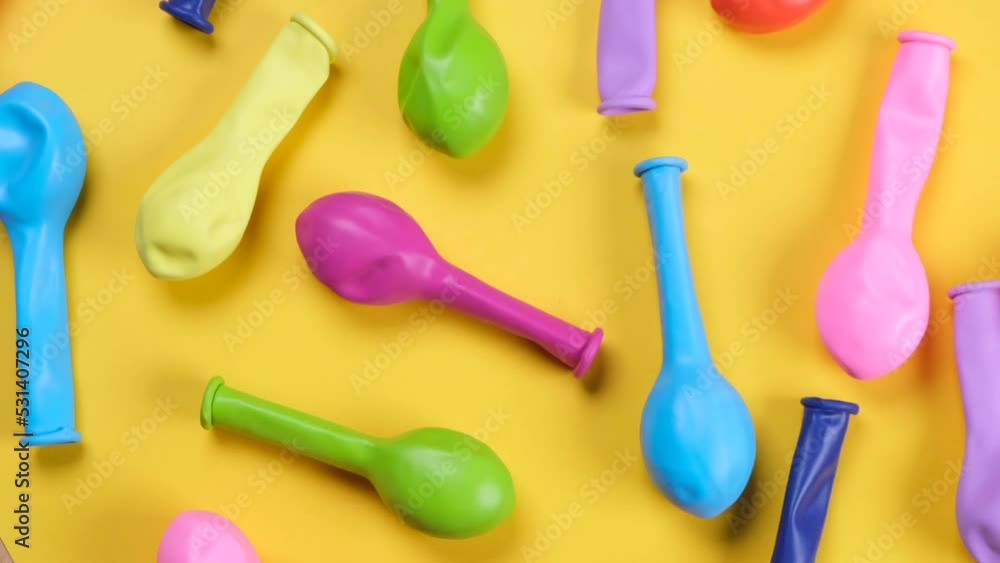 Rotating multi-colored balloons on a yellow background, top view, the concept of celebrating a birthday, party or anniversary Rotating multi-colored balloons on a yellow background, top view, the concept of celebrating a birthday, party or anniversary
