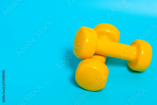 Yellow dumbbells on a blue background, copy space. The concept of fitness, healthy lifestyle, sports, weight loss.