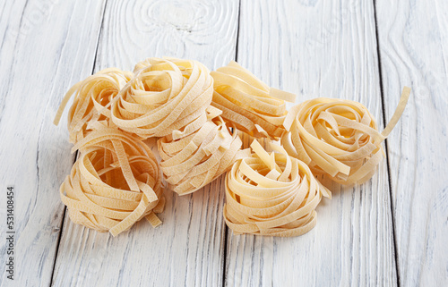 Uncooked tagliatelle pasta on white wooden backgrond
