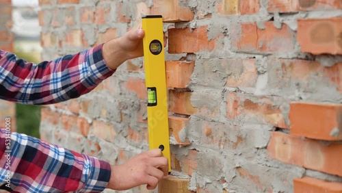 Worker control brick wall using level tool, close up photo