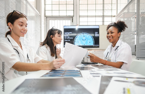 Diverse group female doctors meeting looking at medical x-ray then diagnosis and discussing before surgery at hospital. Surgeon and radiologist teamwork talking, analysis x-ray film before treatment.