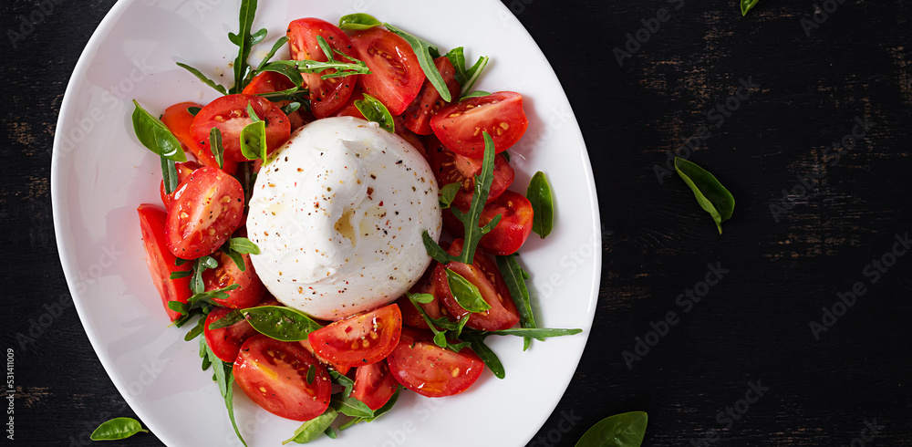 Salad with tomatoes and burrata cheese with basil and olive oil on plate. Italian food. Top view, flat lay