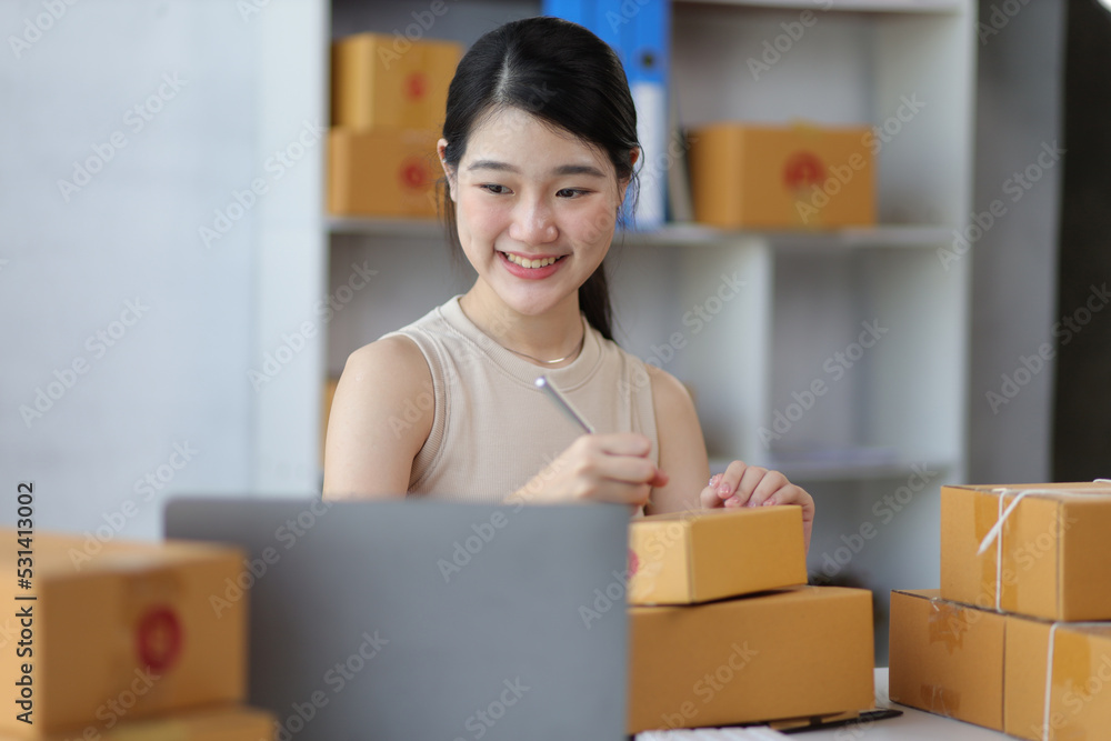 Young Asian woman starting a small business at home is working on cardboardbox preparing to pack products for delivery on internet orders. Small business startup. Young Asian woman starting a small business at home is working on cardboardbox preparing to pack products for delivery on internet orders. Small business startup.
