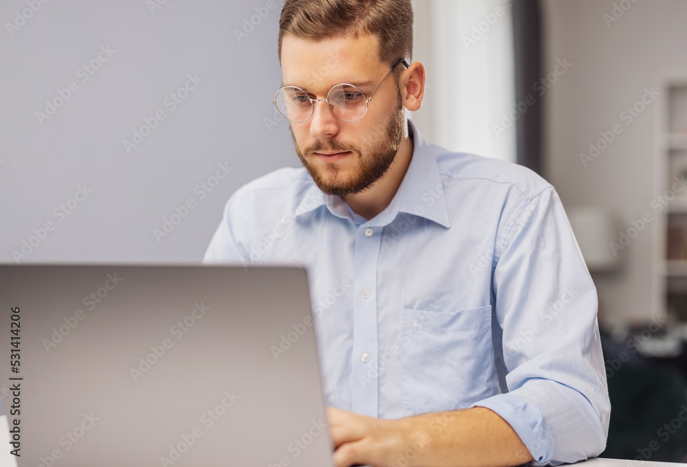 Young focused bearded businessman working on laptop, concentrated on project Young focused bearded businessman working on laptop, concentrated on project