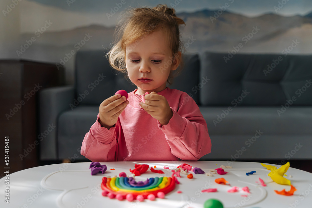 A little girl playing with rainbow from play dough for modeling. Art Activity for Kids. Fine