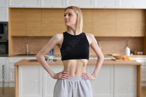 Skinny woman sucking in her belly and standing in the kitchen photo