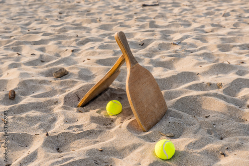 Two wooden rackets and tennis balls in a golden sandy beach on a beautiful summer day.