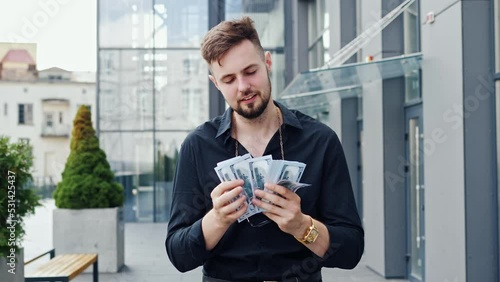Happy successful businessman with an expensive watch and glasses on a strap counts bills of american dollars, waves, walking in business district. Celebrate winner success in betting stock market. photo