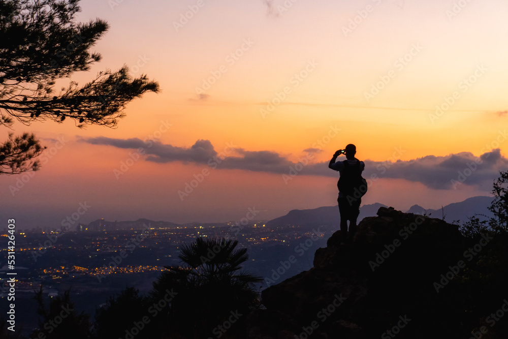 Landscape, silhouette of a boy on a rock photographing the landscape at sunset