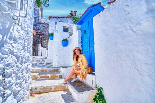 Girl traveler wearing dress and hat walks on an old beautiful street with white houses and blue doors in a European city © Goffkein