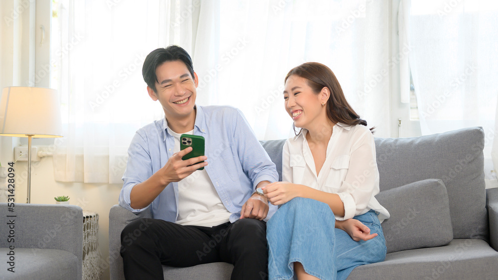 Young smiling asian couple using smartphone in living room at home Young smiling asian couple using smartphone in living room at home