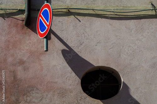 Un caretello che indica il divieto di parcheggio lascia la sua ombra su un muro colito dal sole photo