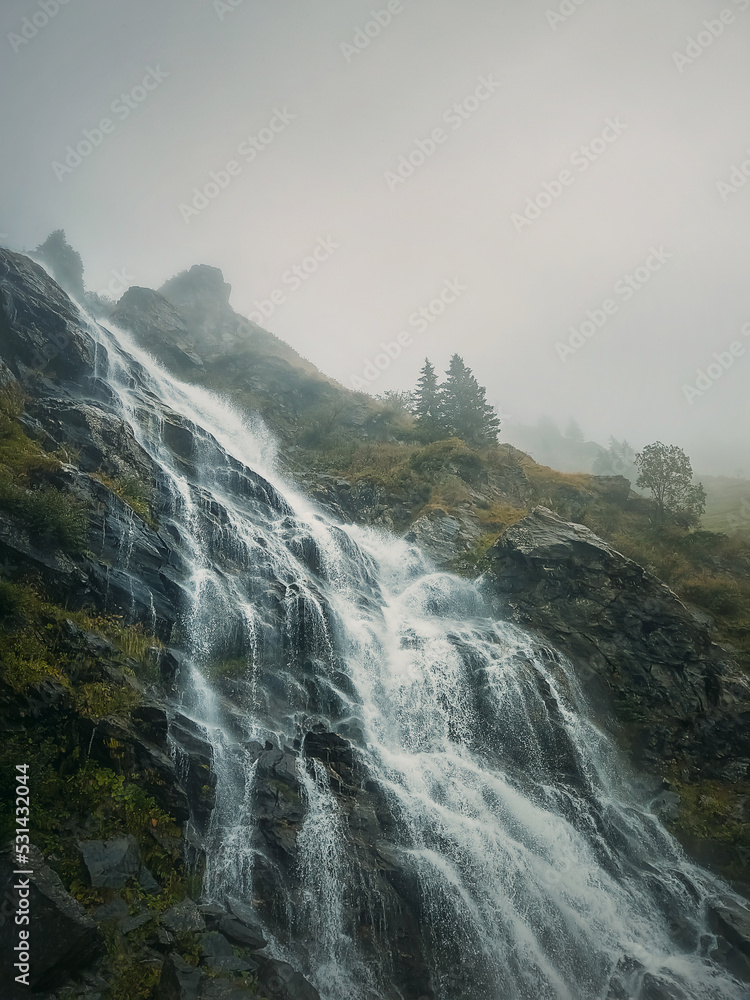 Capra waterfall on the Transfagarasan winding route of Carpathian mountains, Romania. Wonderful landscape with a tumultuous river flowing down through the cliffs in a foggy autumn morning