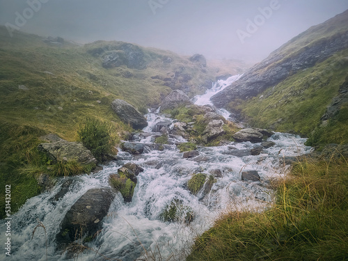 Fast stream flowing across a rocky valley in Fagaras Mountains. River with waterfalls and dense mist landscape
