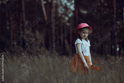 Fototapeta Naklejka Na Ścianę i Meble -  Little angry girl in a pink hat walks in a flowering summer meadow