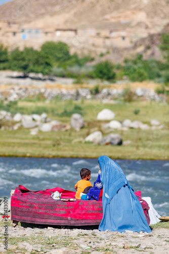 Afghan woman wearing a blue burka (burqa) and her son having tea in the countryside, near Bamiyan (also spelled Bamian or Bamyan), Afghanistan photo
