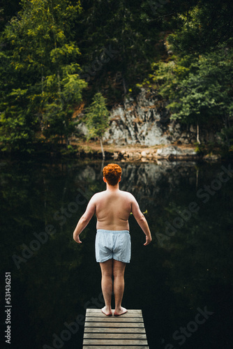 Rothaariger junger mann steht auf einem Steg im Wald und will in das Wasser im See springen