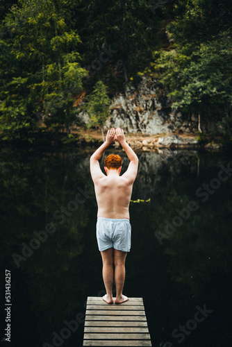 Rothaariger Junge steht auf einem Steg im Wald und will in das Wasser im See springen